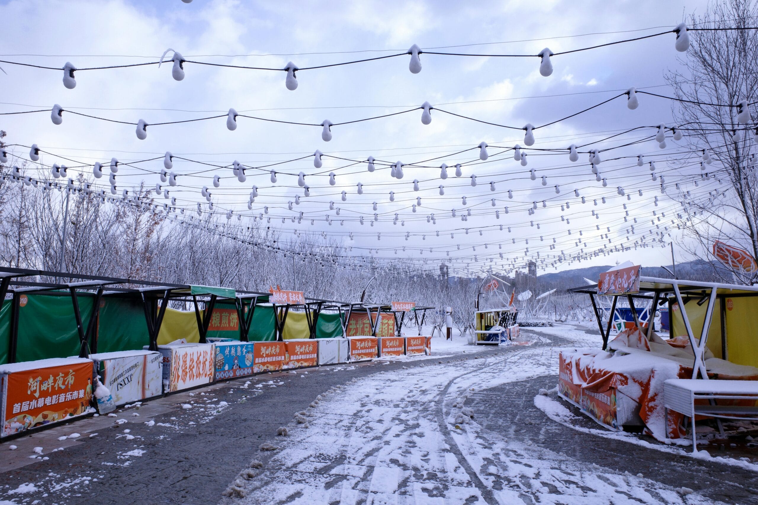 A snowy, deserted outdoor market with string lights on a winter day.