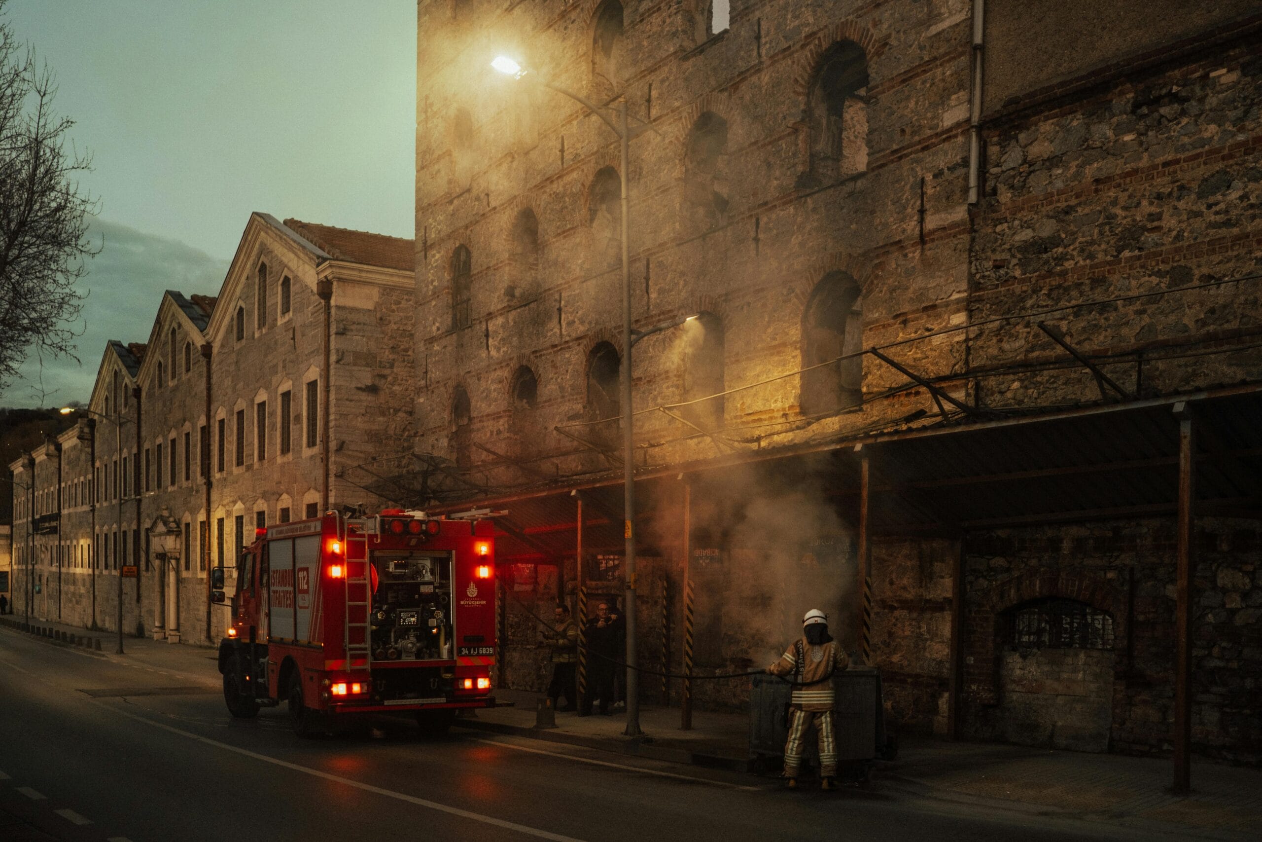 Firefighters managing smoke outside a historic building at dusk. Urban emergency response in action.