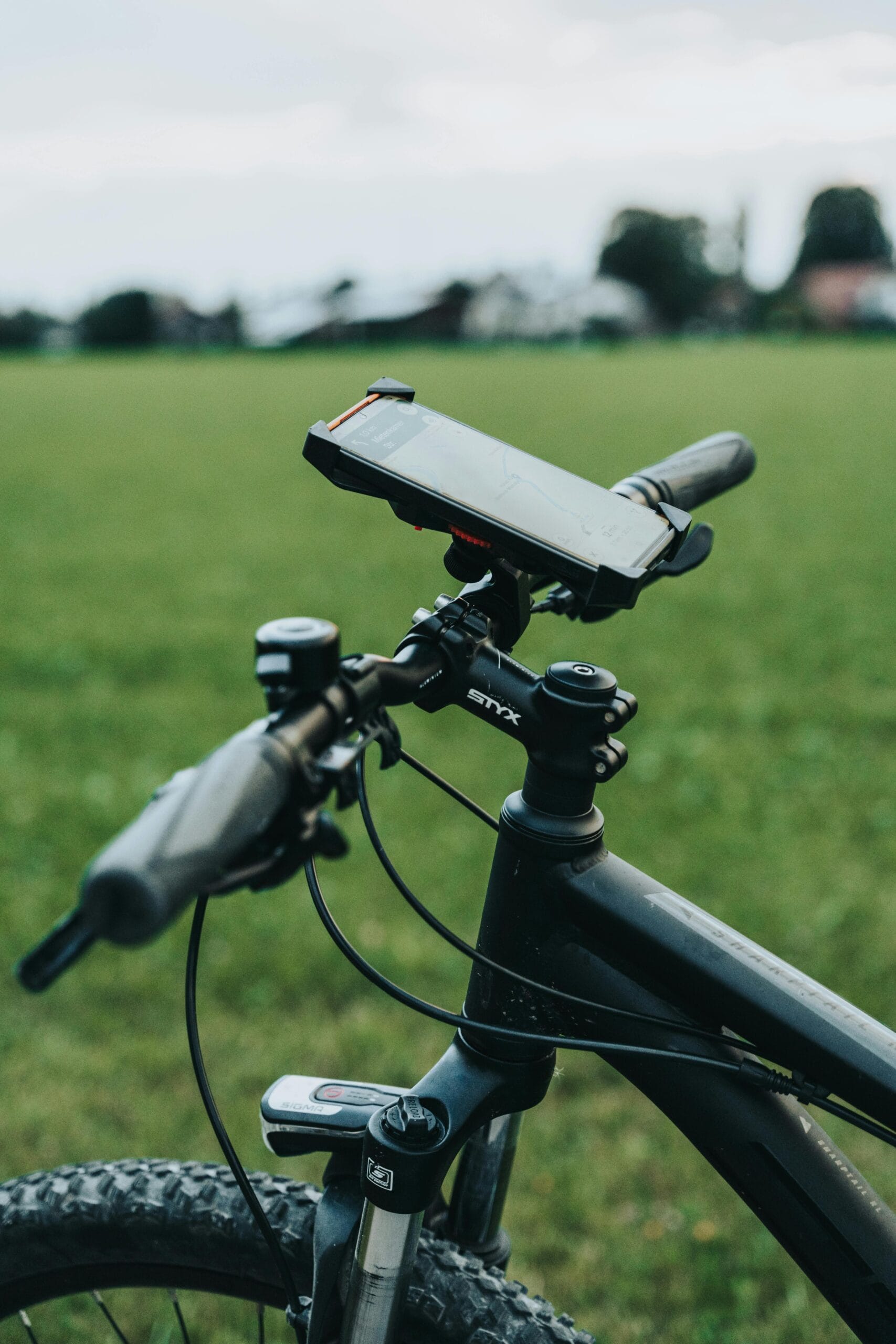 Close-up of a bicycle handlebar with smartphone mount in grassy field, ideal for navigation.