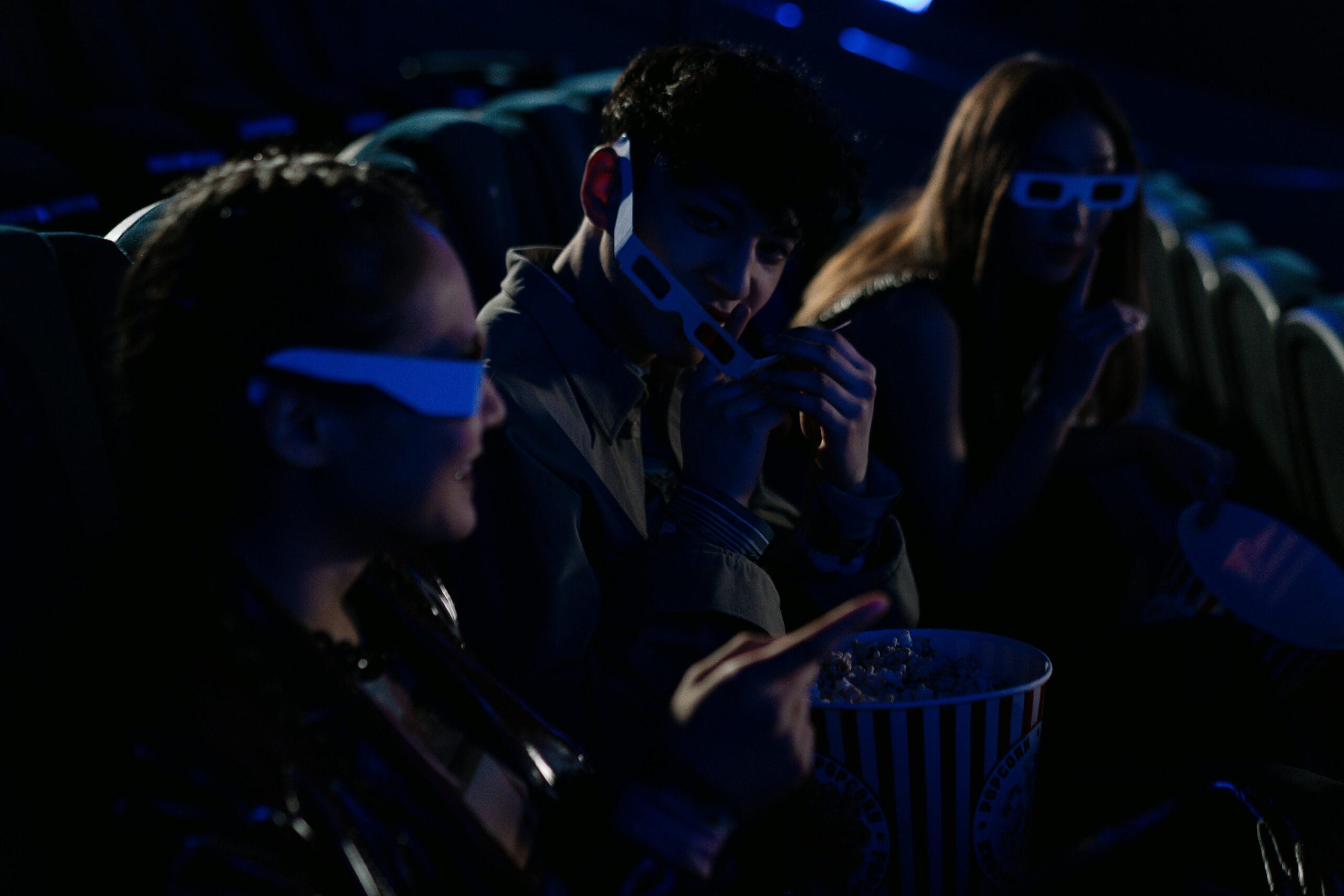 Friends wearing 3D glasses enjoy popcorn and movies in a cinema theater.